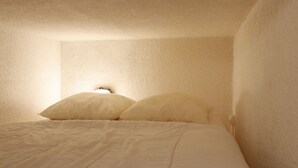 Une chambre avec un lit simple, deux oreillers et une table de chevet avec une lampe.