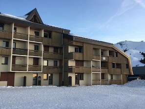 Un hotel a più piani con balconi, una pista da sci sullo sfondo e un paesaggio innevato.