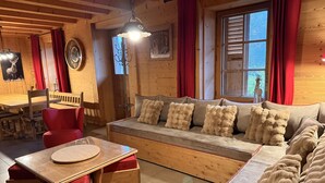A cozy wooden interior with a sofa, red chair, wooden table, and a window with curtains.