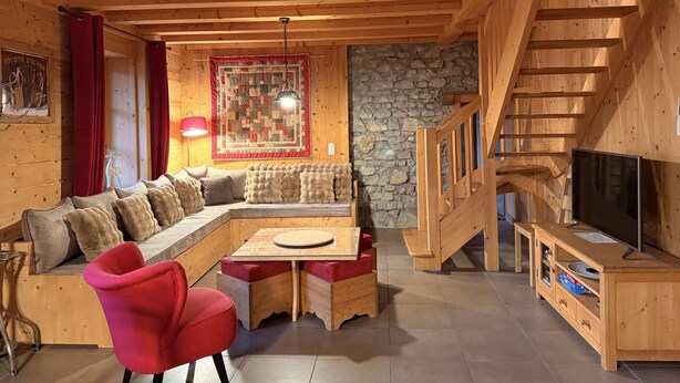 A cozy wooden cabin interior with a wooden staircase, a sofa, a red chair, and a television.