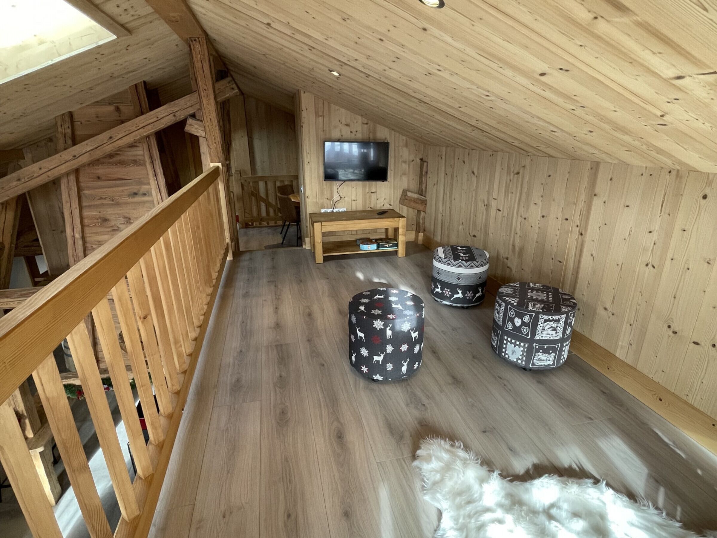 A wooden interior with a TV, wooden bench, and patterned ottomans.