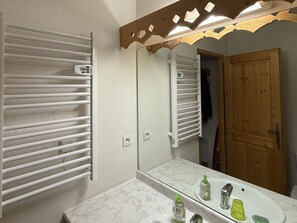 Un baño con lavamanos blanco, espejo y toalleros.