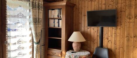 A wooden-paneled room with a bookshelf, a table with a lamp, a chair, and a television mounted on the wall.