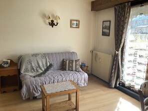 A cozy room with a sofa, a small wooden table, a radiator, and a window with curtains. - Cozy apartment for 2 with Wifi in Samoëns (Samoëns)