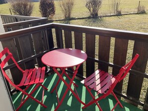 A wooden deck with a green artificial turf, a red table, and two red chairs.