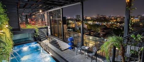 Una piscina interior con vistas a la ciudad, rodeada de paredes de cristal y mobiliario exterior.