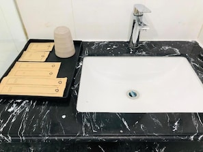Een badkamer met een zwart marmeren wastafel, een witte kraan en een zwarte dienblad met handdoeken en een fles.