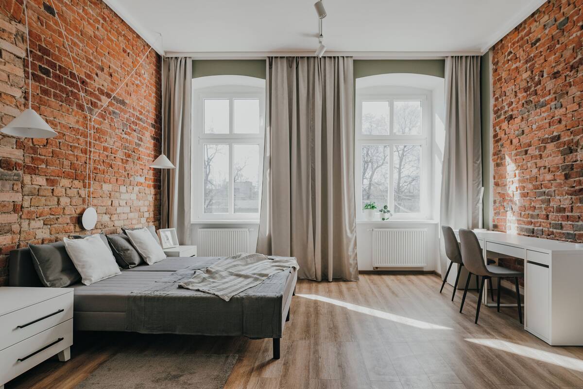A bedroom with a brick wall, a bed, a desk, and a chair.