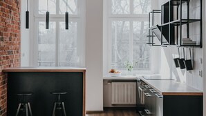 Une cuisine moderne avec un mur en briques, de grandes fenêtres et des tabourets de bar noirs.