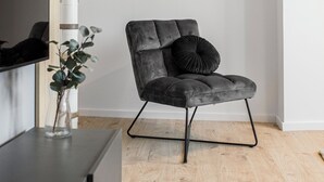 Un salon moderne avec un escalier en colimaçon en bois, un fauteuil gris avec un coussin noir et un vase en verre contenant des plantes vertes.