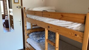 A bunk bed room with a wooden frame, a door with a mirror, and a tiled floor.
