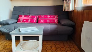 A grey sofa with two red pillows, a small white table with a woven placemat, and a wooden cabinet above.