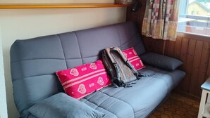 A grey sofa with two red pillows, a wicker basket on a shelf, and a window with curtains.