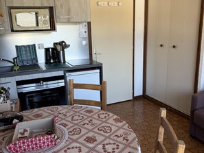 Cocina equipada con microondas, cafetera y refrigerador. Se observa una mesa de comedor con mantel estampado y una silla.
