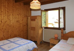 A wooden room with two beds, a wooden wardrobe, a window with a view, and a lamp on a nightstand.