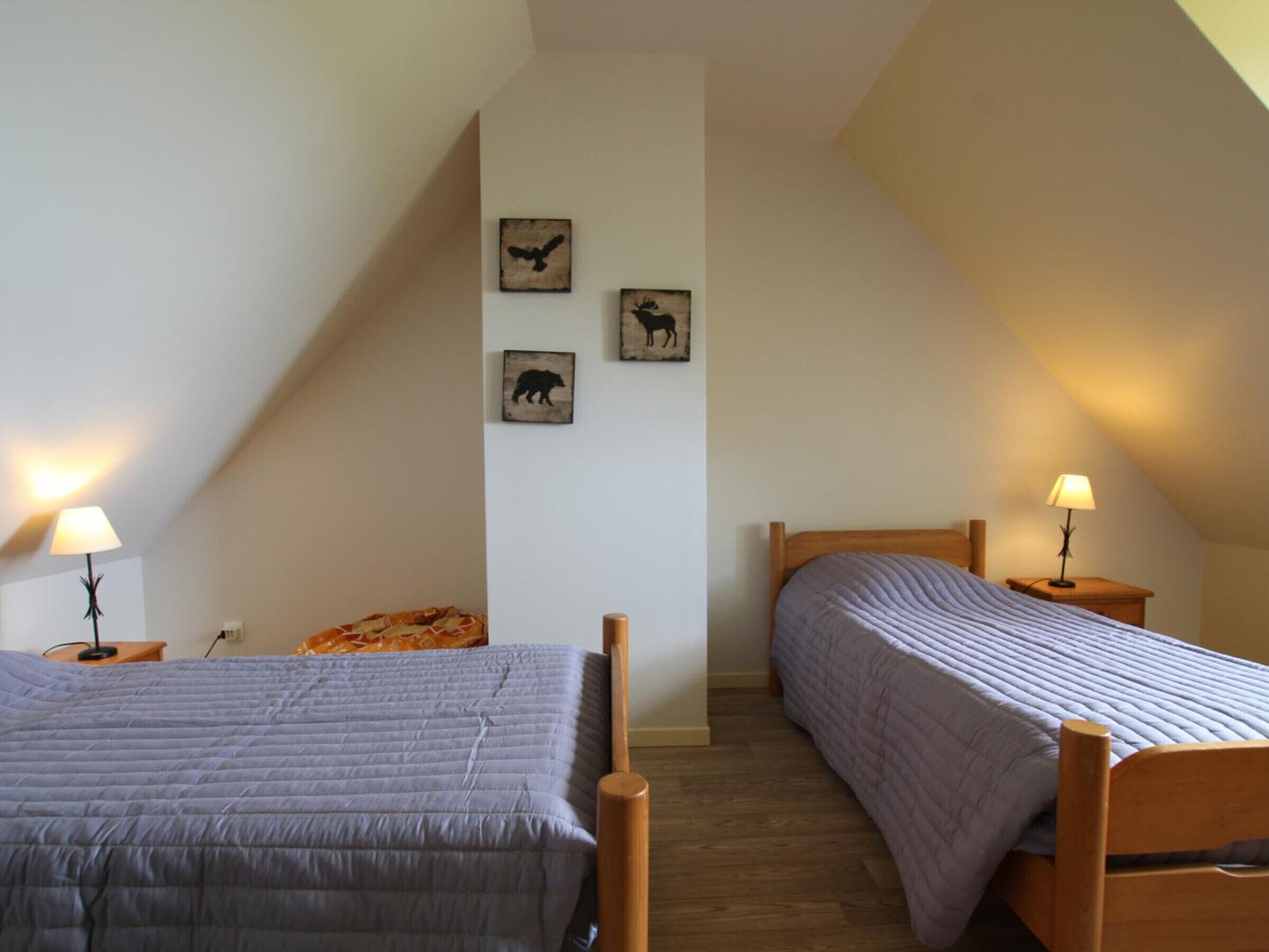 Un dormitorio con dos camas, techo inclinado y tres cuadros con motivos de animales.