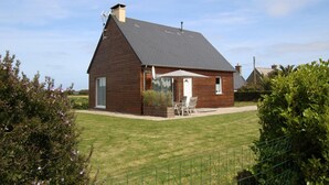 Ein eingeschossiges Haus mit Satteldach, Schornstein und einer Terrasse mit Gartenmöbeln.