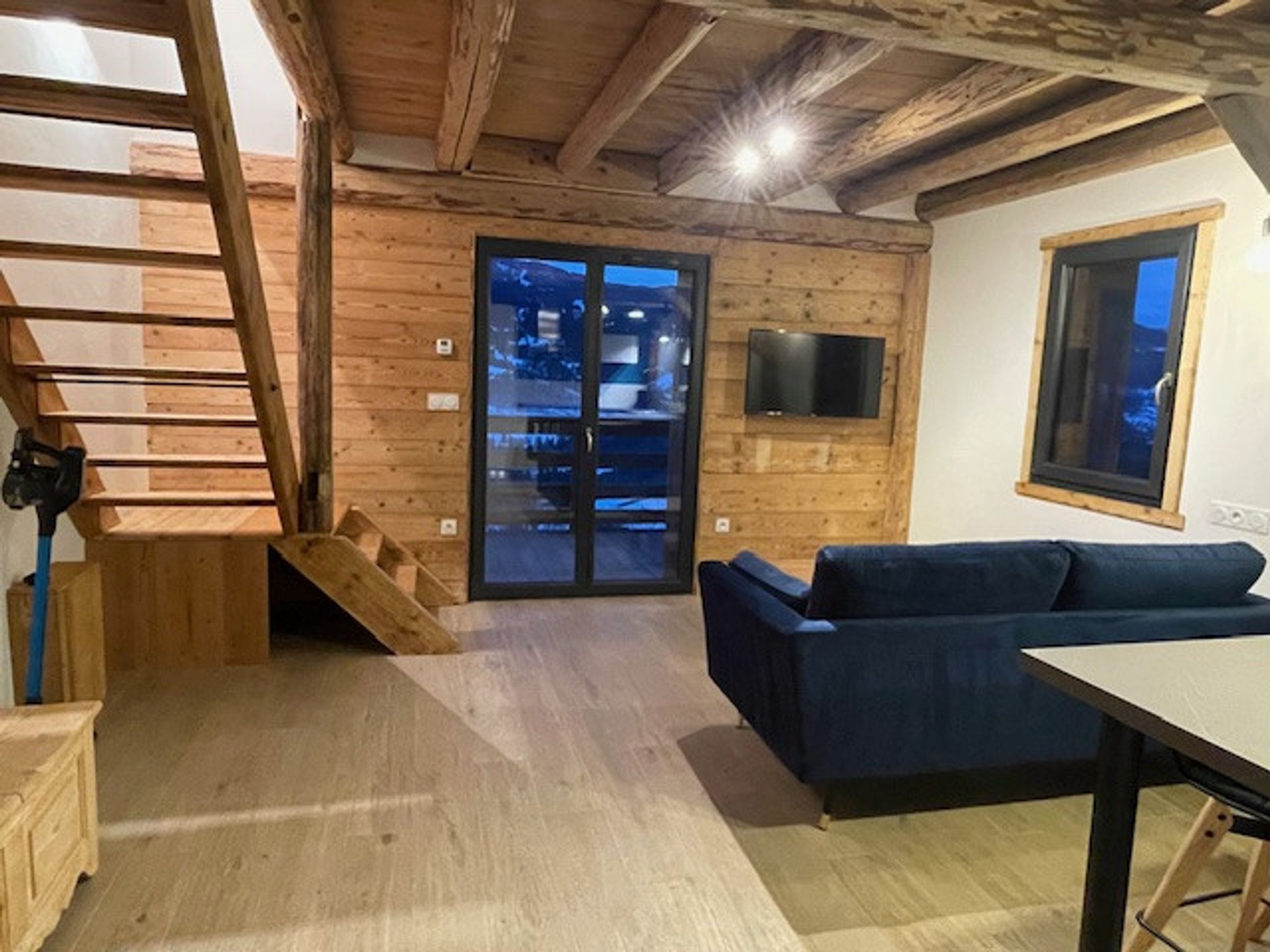 A wooden interior with a staircase, a blue sofa, a television, and a window.