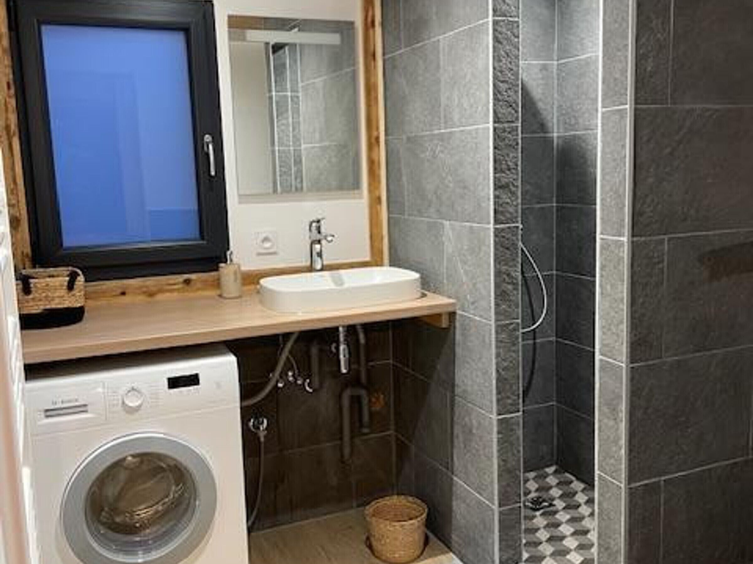 A compact bathroom with a washing machine, a sink, and a shower area.