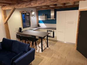 A compact kitchen with a dining area, wooden beams, and a blue accent wall.