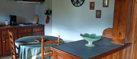 A dining area with a wooden table and chairs, a clock on the wall, and a kitchen in the background.