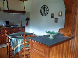 A dining area with a wooden table and chairs, a clock on the wall, and a kitchen in the background.