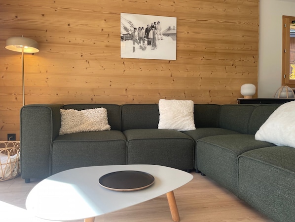 A modern living room with a sectional sofa, a white coffee table, and a wooden wall.