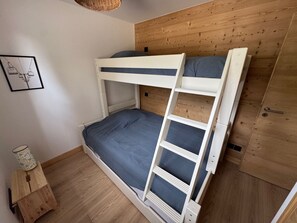A bunk bed with a ladder, a small wooden table with a lamp, and a wooden wall panel.