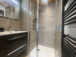 A modern bathroom with a glass shower enclosure, a vanity with a mirror, and a towel rack.