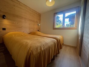 A room with two beds, wooden walls, a window, and a light fixture. - Spacious apartment in Samoëns - 8 people with Wifi (Samoëns)