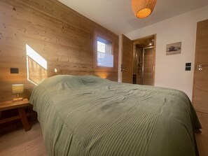 A wooden-paneled room with a bed, a nightstand, a window, and a door leading to a shower.