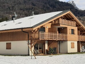 A wooden chalet with a balcony, a ski lift in the background, and a snowy mountain landscape.