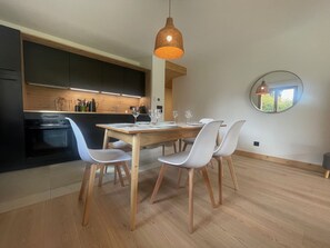 A modern kitchen with dark cabinets, a wooden dining table, and white chairs.