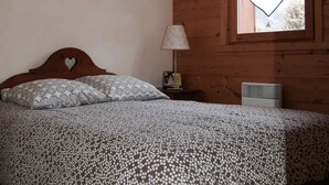 Un dormitorio con cabecera de madera, cama con ropa de cama estampada, mesita de noche con lámpara y ventana decorada con un adorno con forma de corazón.
