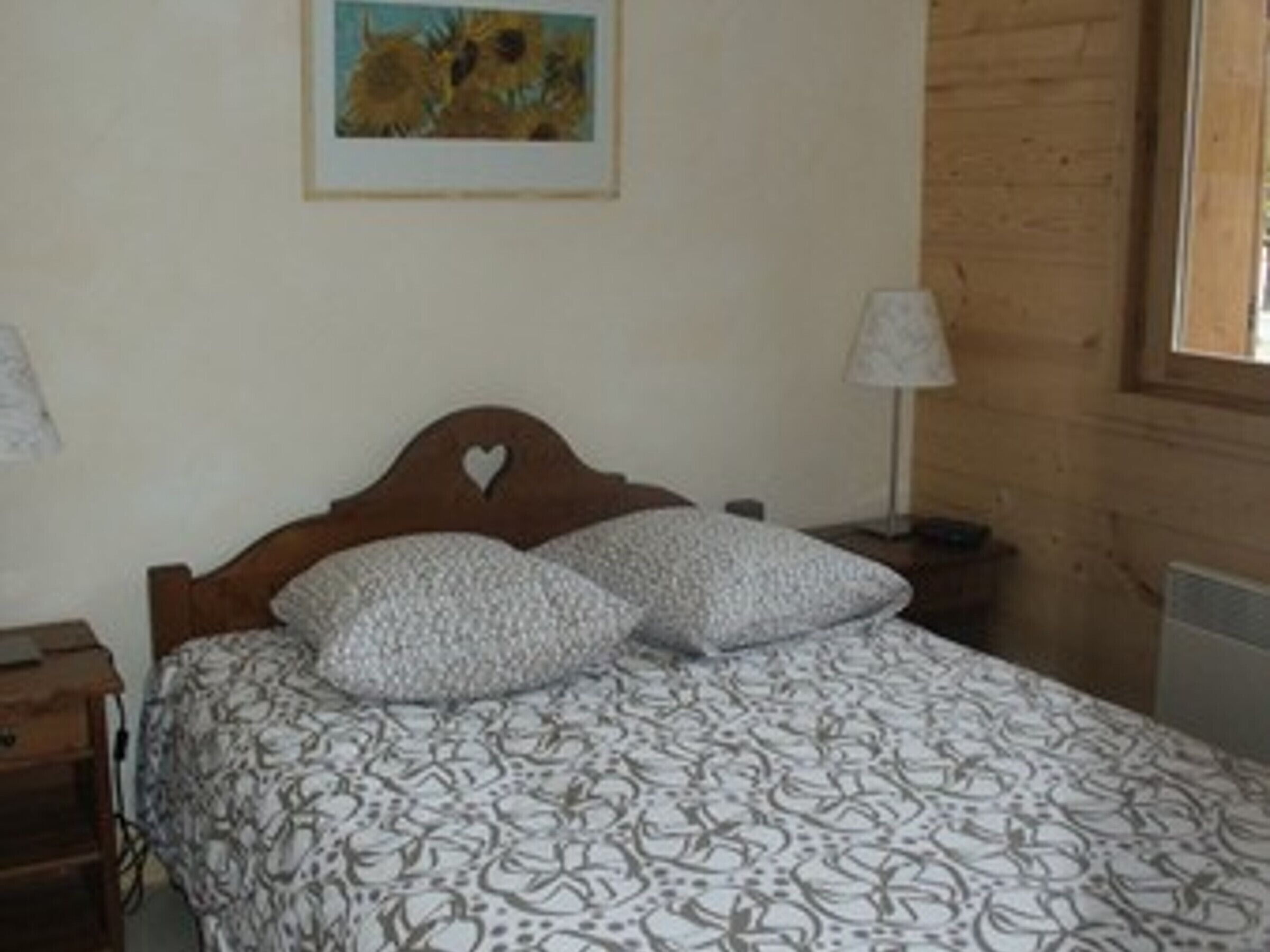 Une chambre à coucher avec une tête de lit en bois, deux oreillers, une couvre-lit à motifs, une table de chevet, une lampe et un tableau encadré au mur.