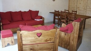 Una habitación acogedora con un sofá rojo, sillas de madera, una mesita de madera y un armario de madera.