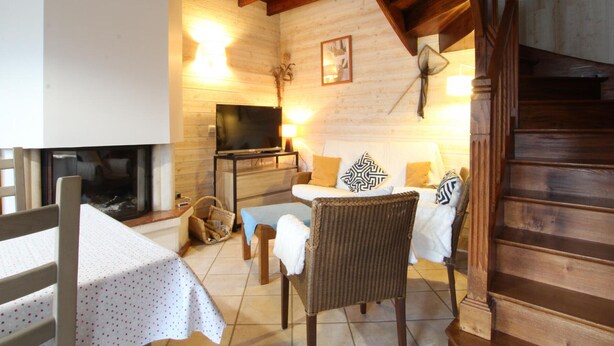 A cozy living room with a fireplace, wooden ceiling, and a television on a stand.