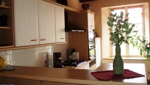 A kitchen with white cabinets, a stove, and a coffee maker. There is a window with a plant on the windowsill.