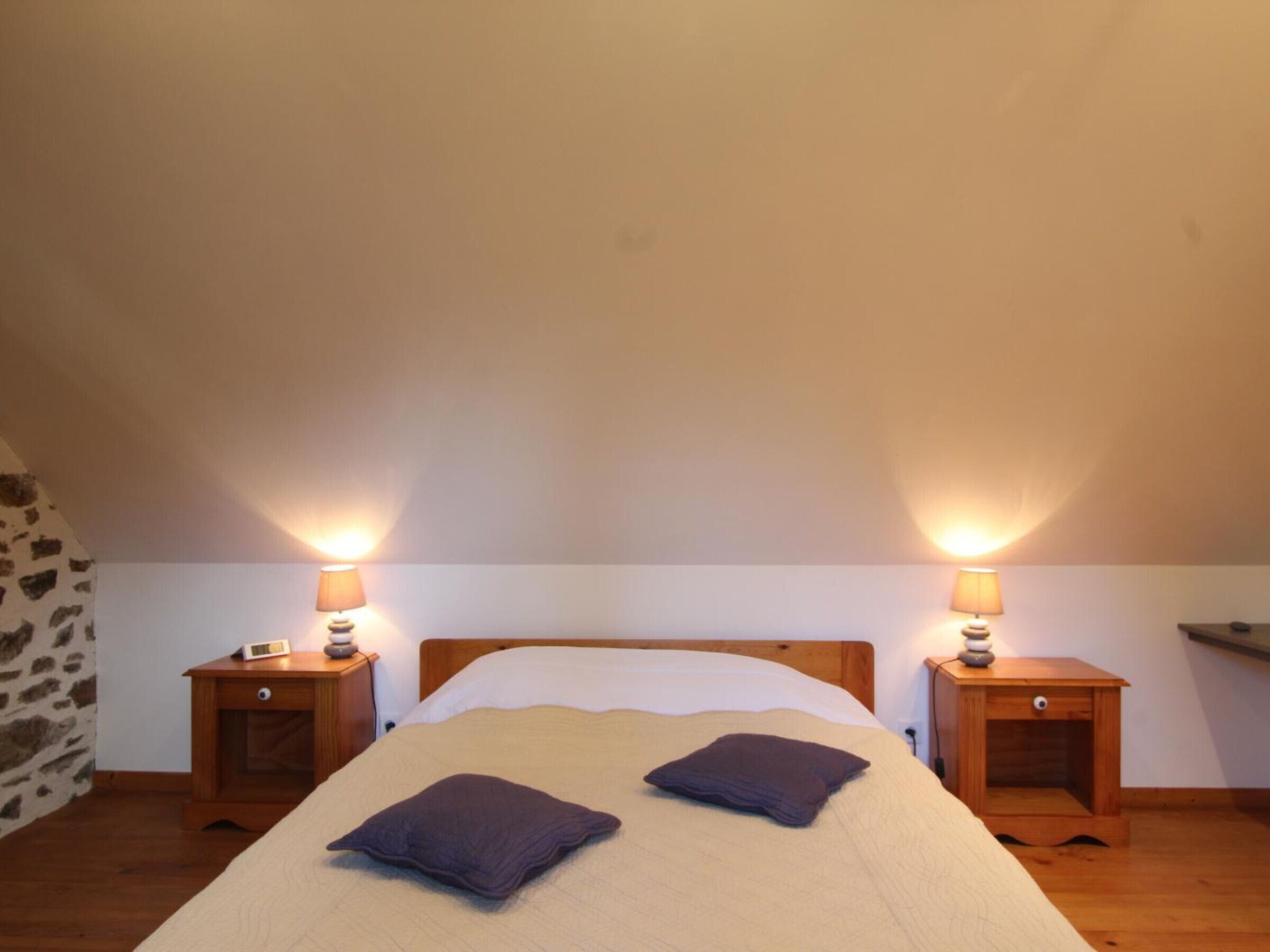 Una cama individual con dos almohadas en una habitación con techos inclinados y dos mesitas de noche con lámparas.