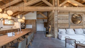 Una cocina amplia con vigas de madera, un comedor con una larga mesa y sillas, y un rincón de estar acogedor con un sofá y cojines.