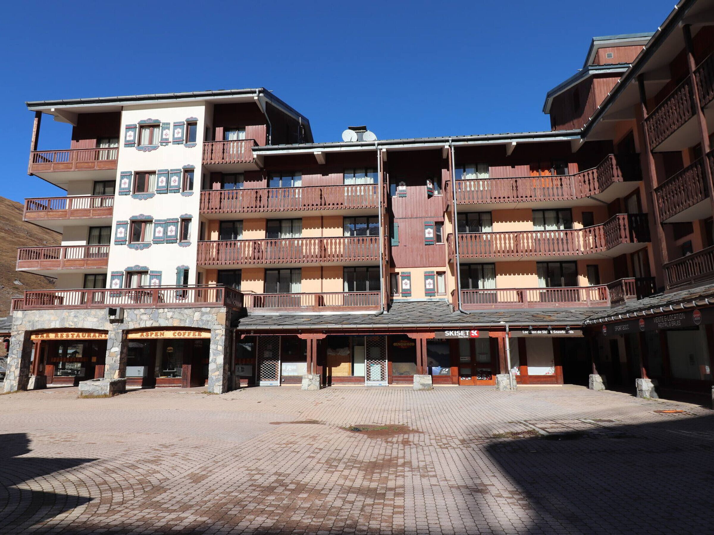Un hotel de varios pisos con balcones, un cartel de estación de esquí y fachada de piedra.