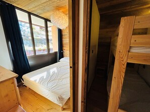 Um quarto de madeira com uma cama, uma janela com cortinas e vista para o exterior.