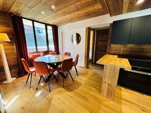 Uma sala de jantar com piso de madeira, uma mesa redonda e cadeiras, uma televisão e um armário de madeira.