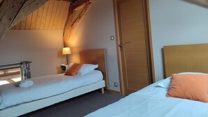 A room with two beds, wooden beams on the ceiling, a wooden door, and a nightstand with a lamp. - Peaceful cottage for 4 guests with garden in Montbeugny (Montbeugny)