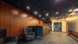 A reception area with a wooden wall, a reception desk, and a seating area with two chairs. - Warsaw Praga Studio – Central Access & Parking (Warszawa)