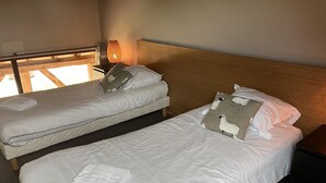 Een hotelkamer met twee eenpersoonsbedden, een houten hoofdbord, een nachtkastje met een lamp en een raam met uitzicht.