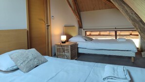 Un dormitorio cálido en el ático con dos camas, techo de madera y una mesita de noche pequeña con lámpara.