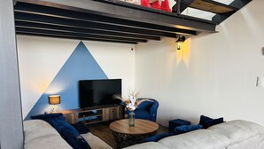 Un salon moderne avec un grand canapé d’angle, une table basse, un téléviseur à écran plat et un vase décoratif.