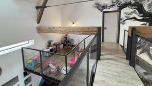 Un espace de vie de style « loft » avec un plafond en pente, des poutres apparentes, une rambarde en verre et une fresque représentant un arbre.