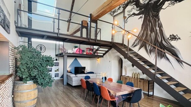 Un espace de vie moderne de style loft, comprenant un coin repas, un escalier et une grande fresque représentant un arbre.